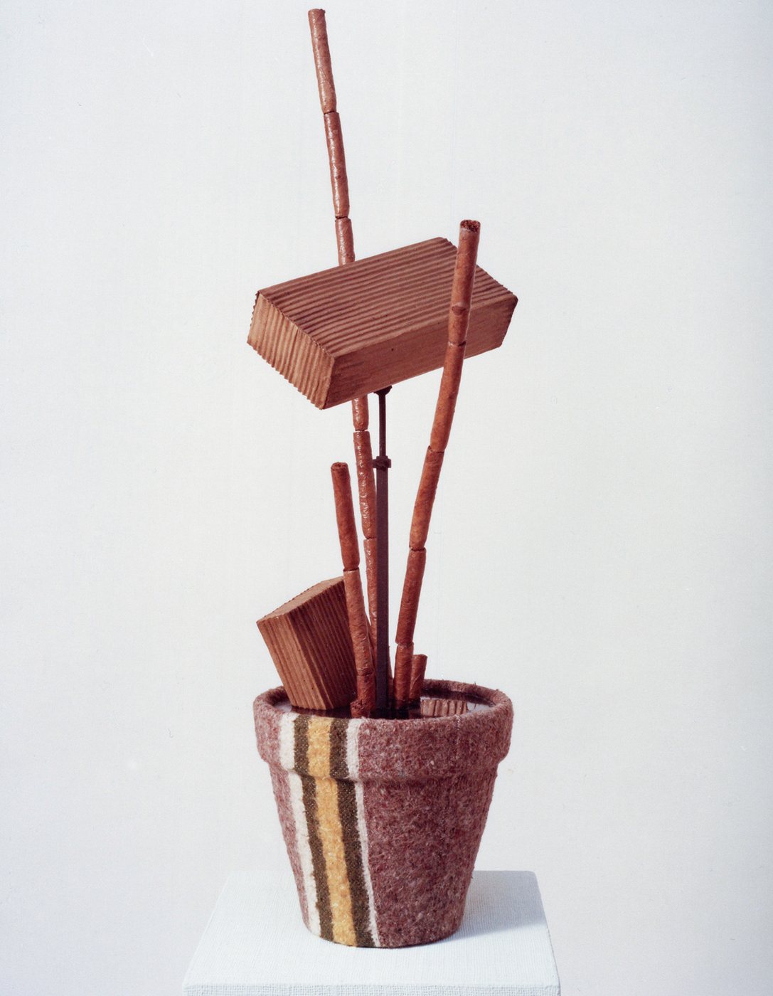 Bogota, 1974 - a marbled pot holding upright reed stems and stacked angular wooden blocks, standing on a white plinth.